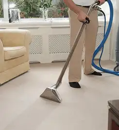 Professional carpet cleaner using a hot-water extraction wand and hose machine in a living room in Louisville, KY.