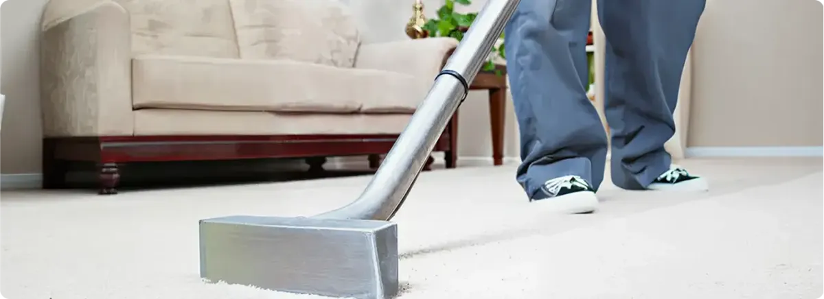 Carpet cleaning technician using a hot-water extraction wand on a light-colored carpet in a living room, Louisville, KY.