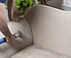 Professional upholstery cleaner deep-cleaning a fabric sofa with a handheld extraction tool and hose in Louisville, KY.